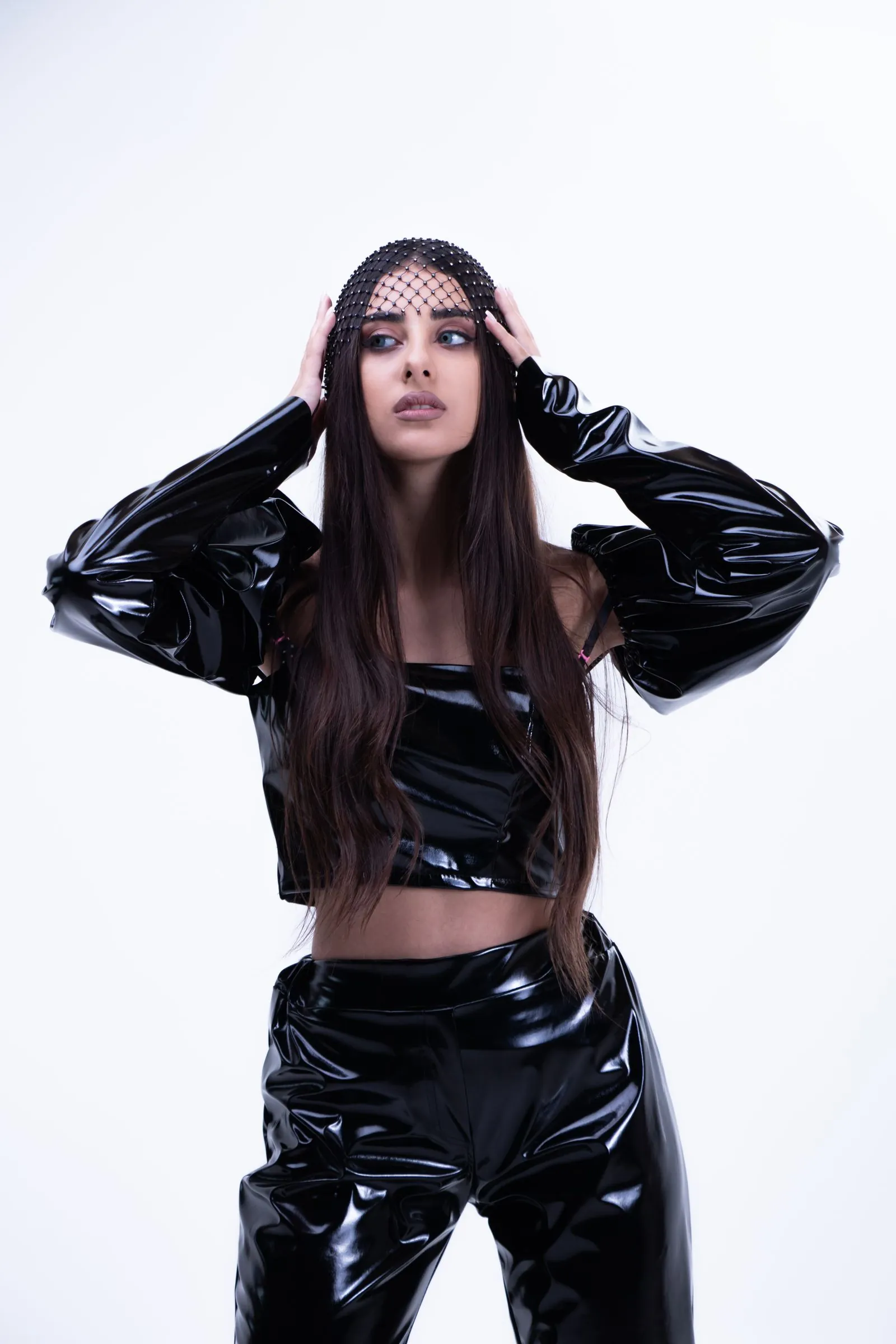 Model in glänzendem schwarzem Lack-Outfit vor weißem Hintergrund